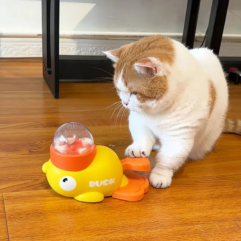 A white and orange cat actively playing with the yellow duck toy by pressing the pedal with its paw