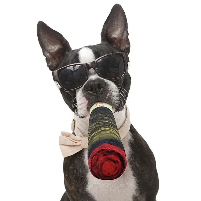 A cool Boston Terrier dog wearing sunglasses and a bow tie, holding the plush cigar-shaped toy in its mouth.