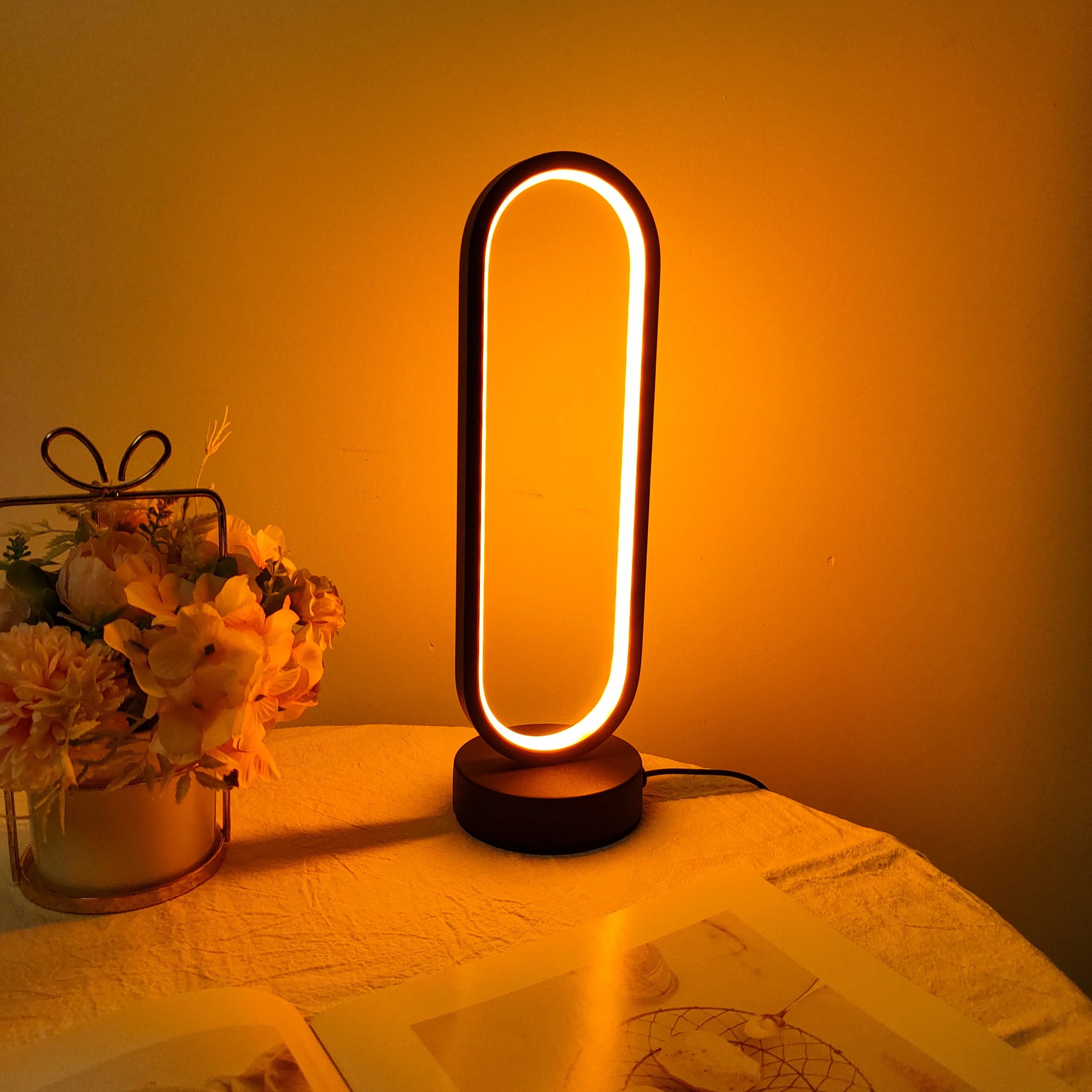 The decorative oval LED ring lamp providing warm ambient lighting in a stylish room setting.