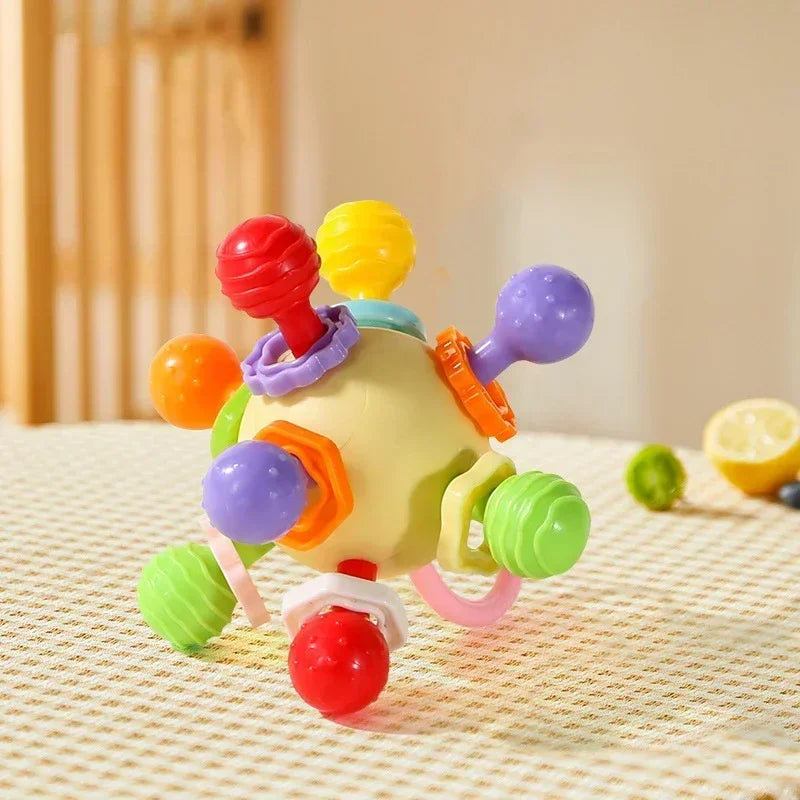 The yellow and purple version of the silicone sensory rattle toy on a checkered surface.