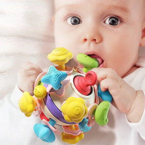 A close-up of a baby chewing on a colorful, multi-textured soft silicone rattle cube, designed for teething relief.