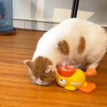 A close-up of a cat nudging the yellow duck treat dispenser with its nose, trying to get the treats inside.