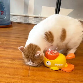A close-up of a cat nudging the yellow duck treat dispenser with its nose, trying to get the treats inside.