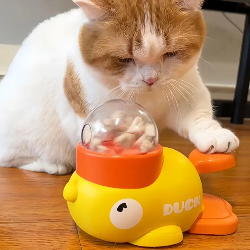 A white and orange cat pressing its paw on the pedal of the yellow PawJoy interactive duck feeder toy.