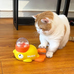 A white and orange cat actively playing with the yellow duck toy by pressing the pedal with its paw