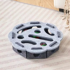 The flower-shaped interactive cat puzzle box in a light and dark grey felt material.