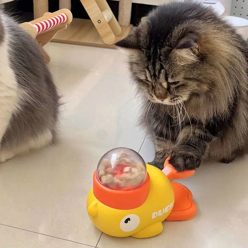 A fluffy, long-haired tabby cat curiously looking at the yellow duck treat dispenser toy.