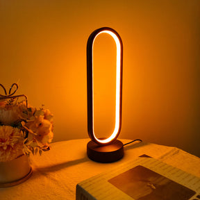 The oval LED desk lamp emitting a warm, inviting glow next to a vase of flowers.