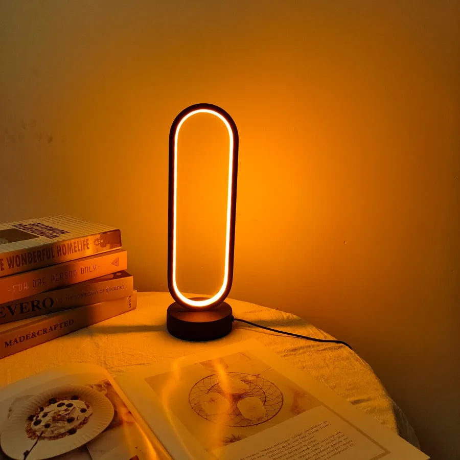 The oval LED table lamp creating a cozy ambient glow on a table with books and a magazine.