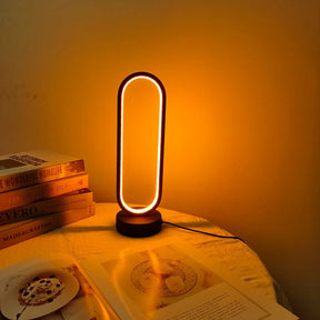 The oval LED table lamp creating a cozy ambient glow on a table with books and a magazine.