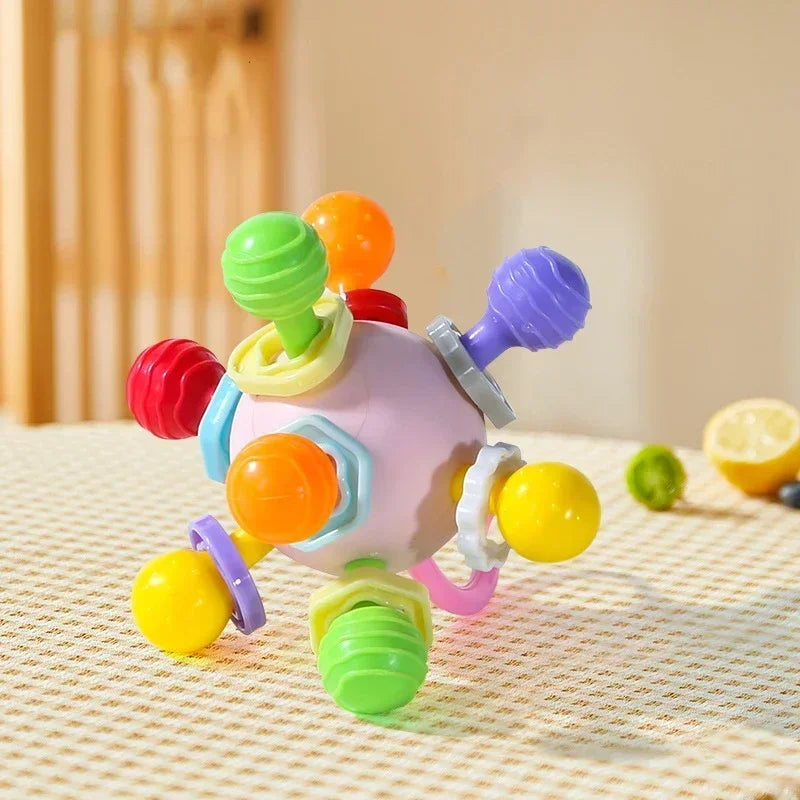 The pink and orange version of the silicone sensory rattle toy on a checkered surface.