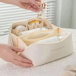 A hand placing a serum bottle into one of the organised compartments of the cream-white LuxeCase makeup bag.