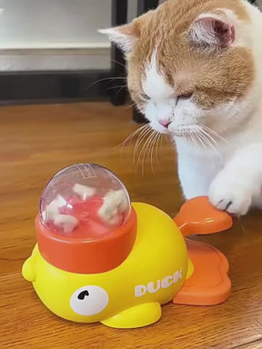 A video showing a cat playfully pressing the pedals of the yellow PawJoy duck feeder toy, which then dispenses a treat from the clear dome on top.