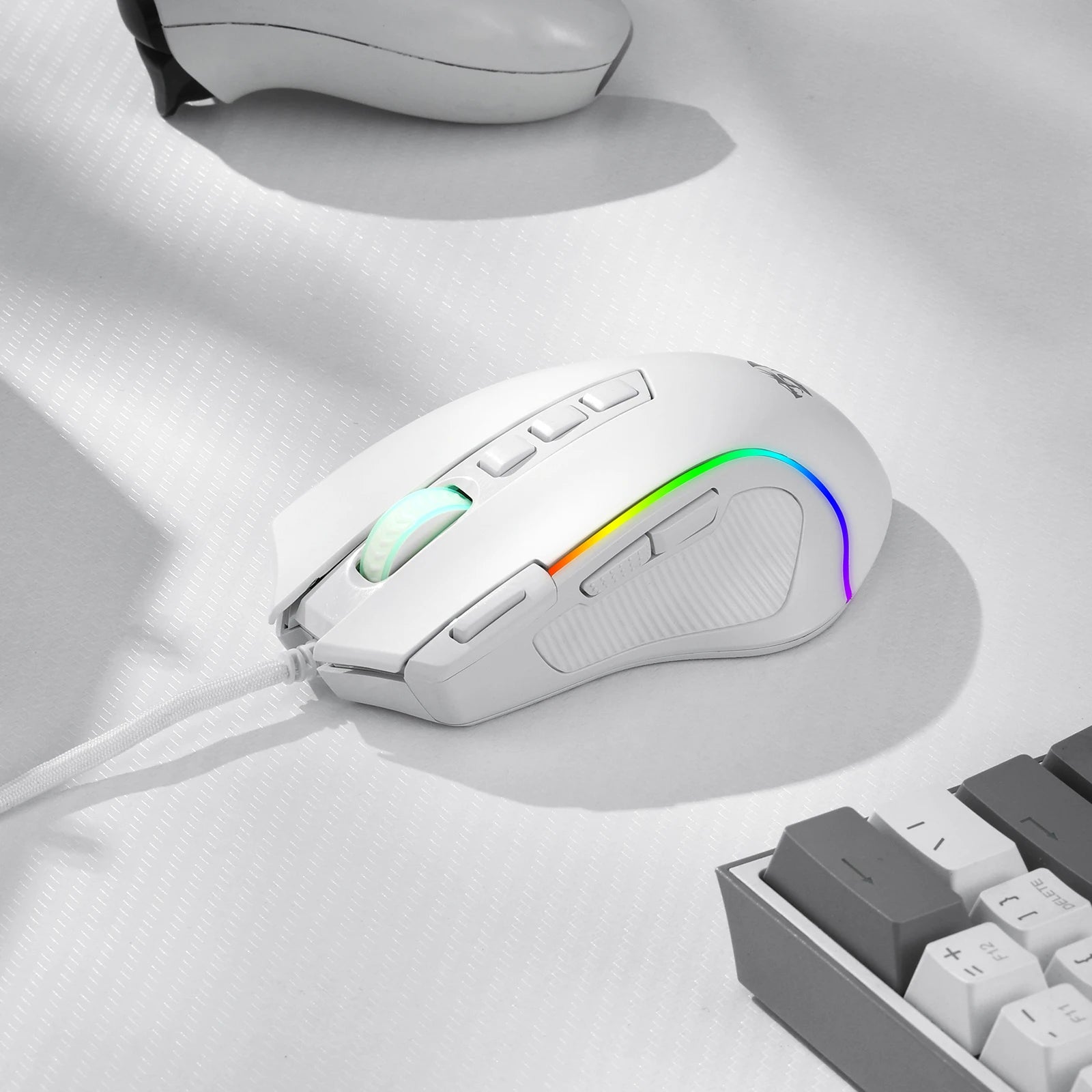The white Redragon M612 gaming mouse on a textured white desk next to a keyboard, showing its RGB lighting.