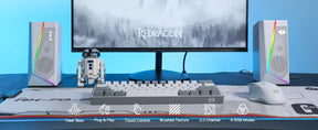 A full gaming desk setup featuring the white Redragon GS520 speakers, a keyboard, mouse, and monitor.