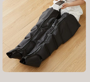 A woman sitting on the floor using the Jinkairui air compression leg massager boots with the controller in her hands.